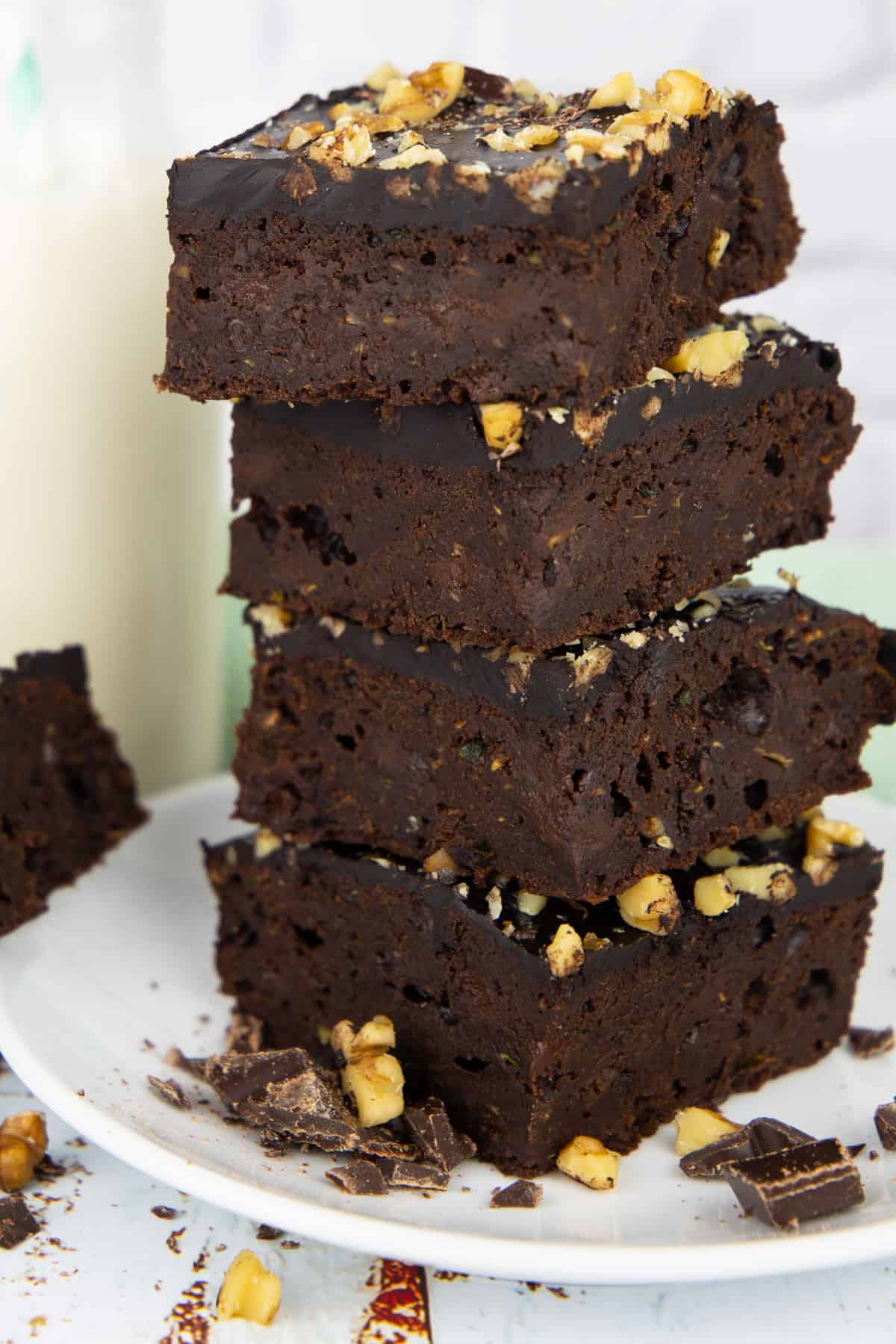 a stack of four brownies on a white plate with chopped chocolate and walnuts on the side