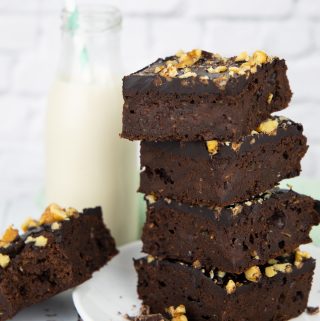 a stack of four zucchini brownies on a white plate with a bottle of milk in the background