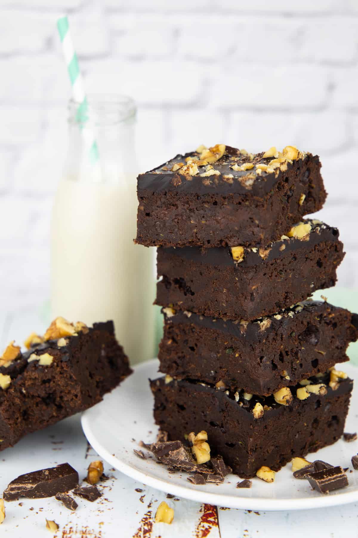 a stack of four zucchini brownies on a white plate with a bottle of milk in the background