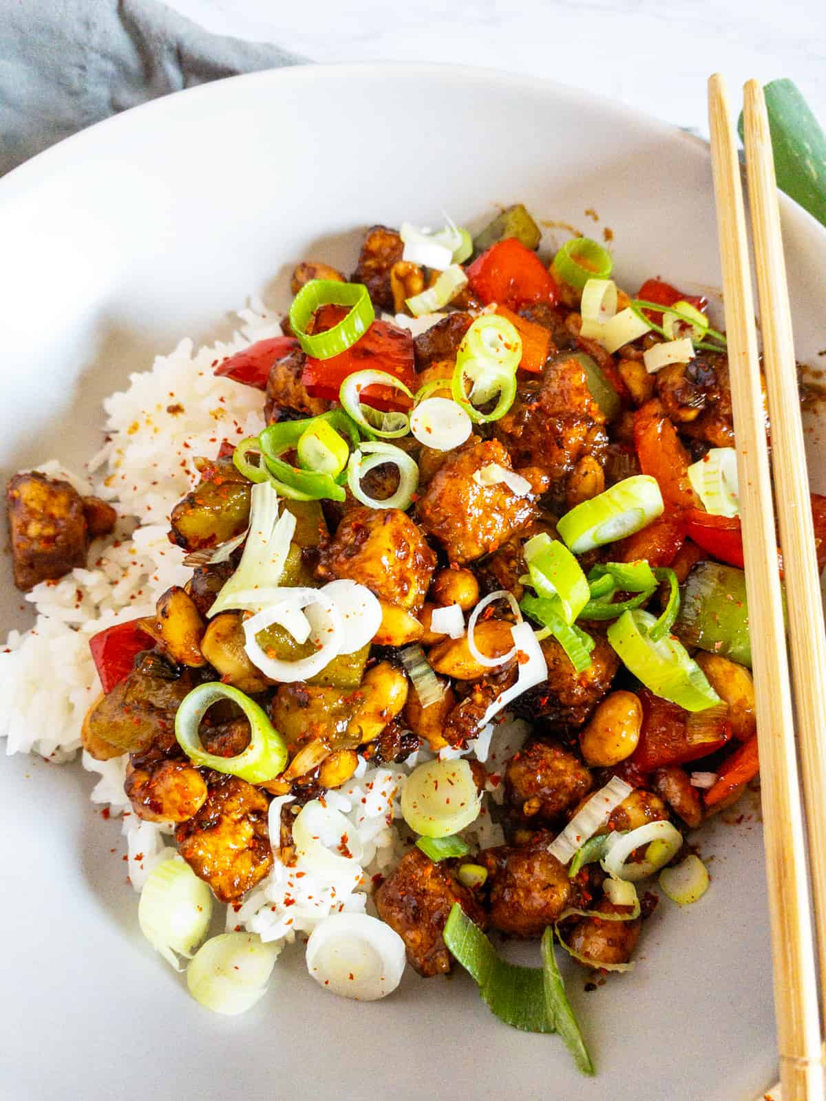 Kung Pao Tofu over rice in a white plate with chop sticks 