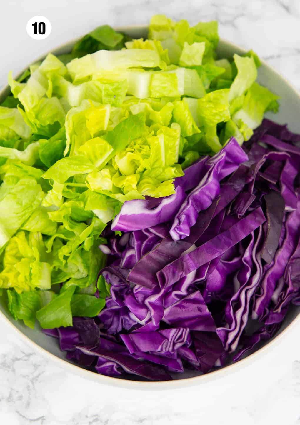 a bowl filled with chopped lettuce and red cabbage on a marble countertop