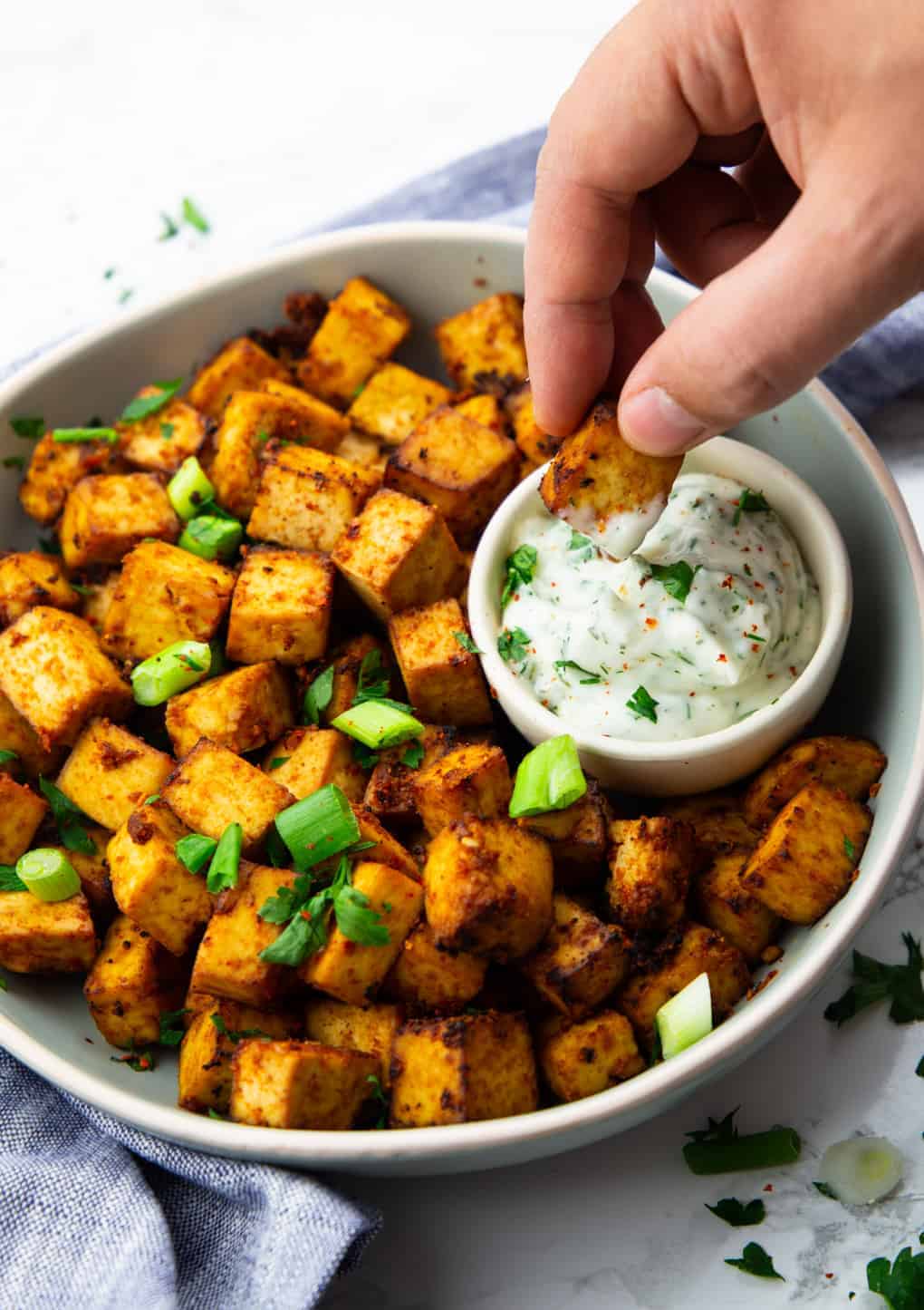 a hand dipping air fryer tofu into a small bowl of vegan ranch sauce 