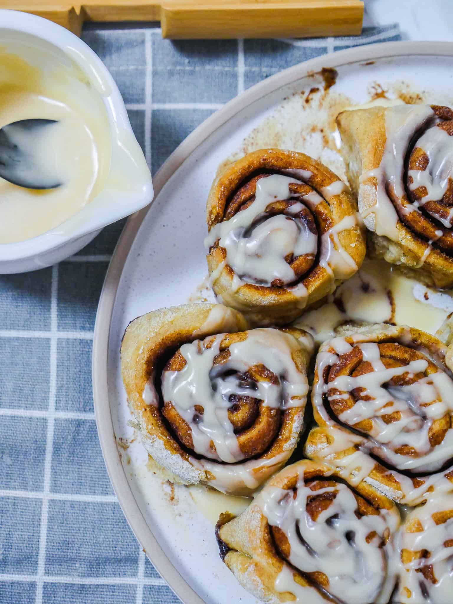vegan cinnamon rolls on a white plate with frosting in a bowl on the side
