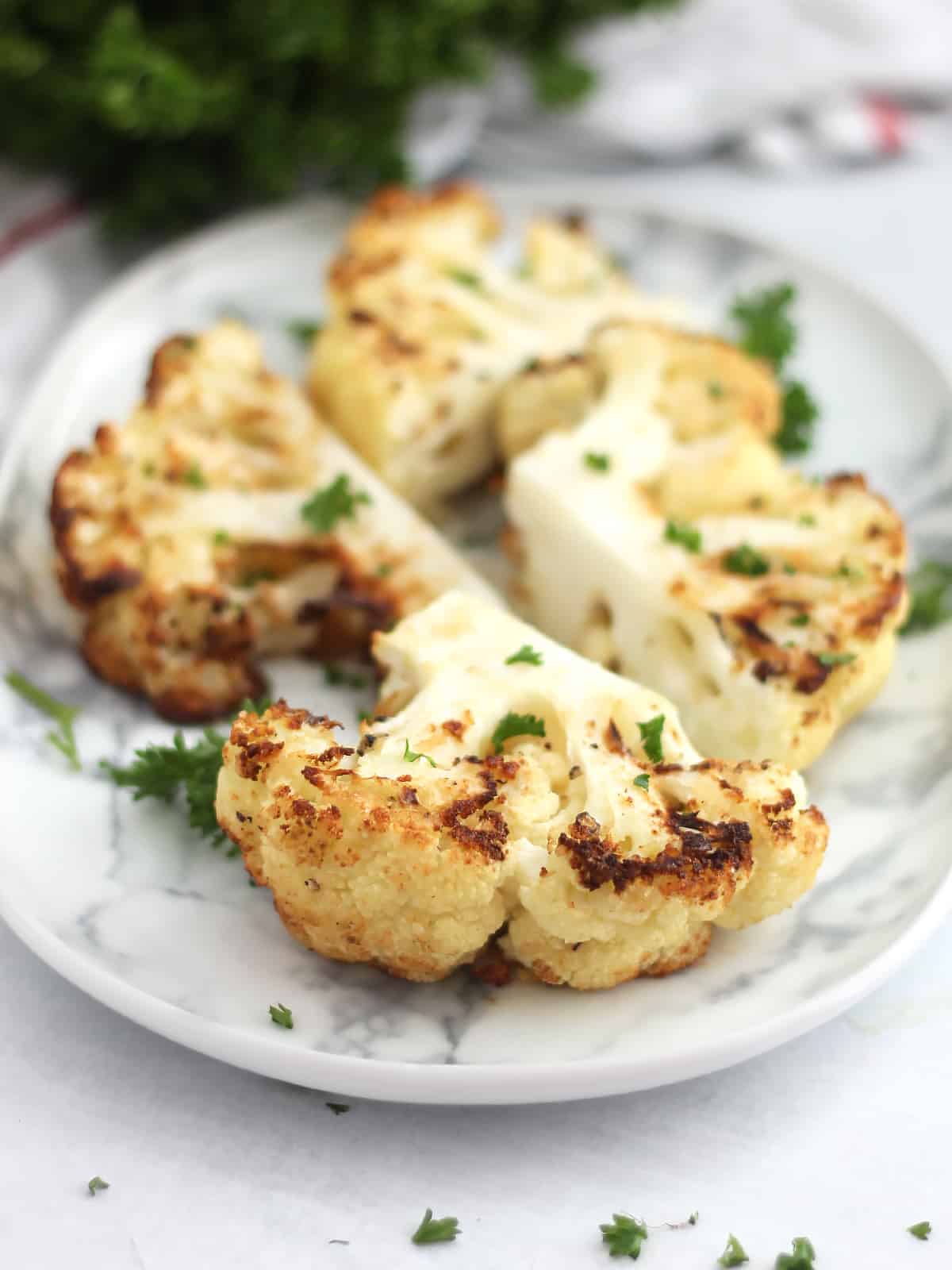 air fryer cauliflower steak on a white plate with chopped parsley sprinkled on top 