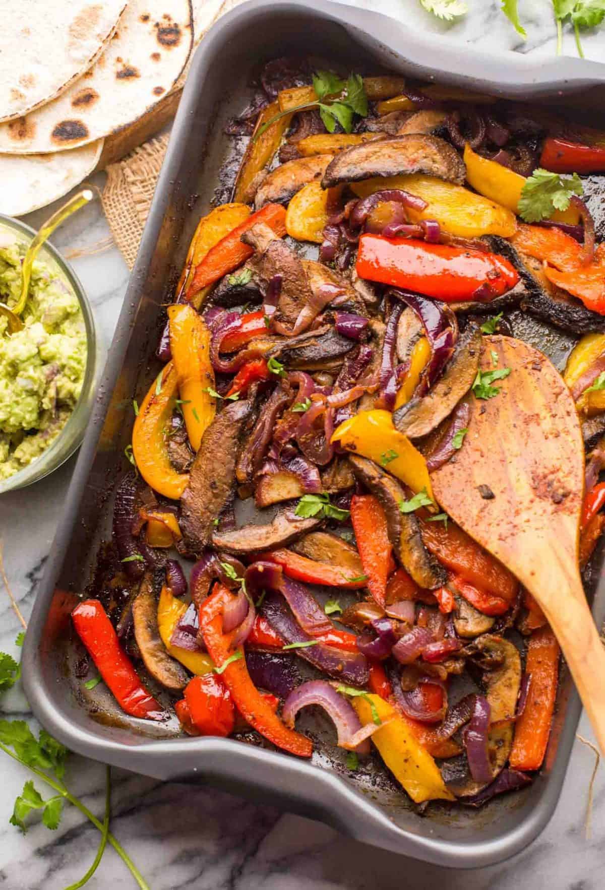 portobello mushroom fajitas on a sheet pan with guacamole and tortillas on the side 