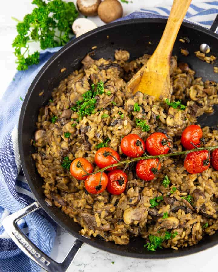 a pan with vegan mushroom risotto topped with roasted cherry tomatoes on a marble countertop 