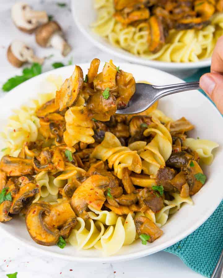 a hand picking up some vegan mushroom stroganoff out of a white bowl 