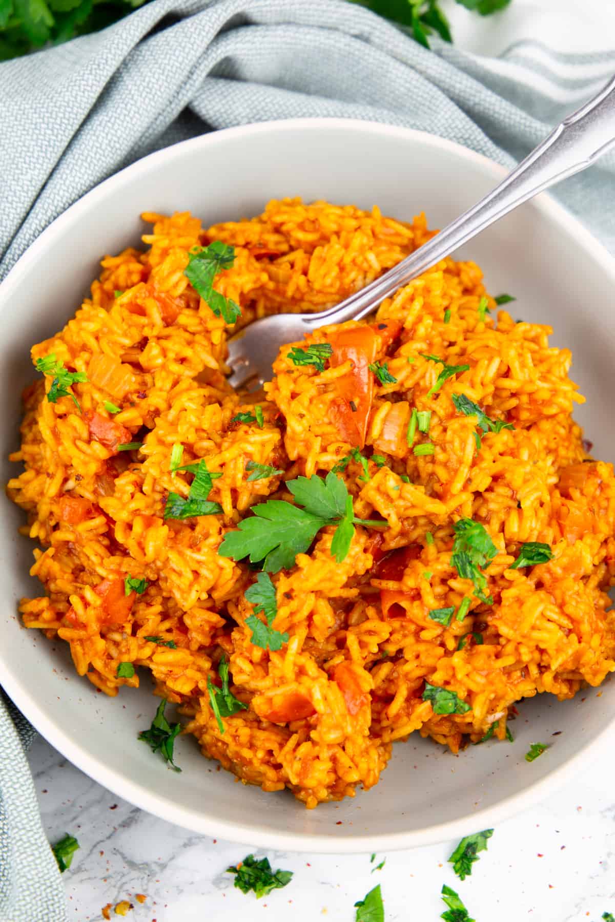 tomato rice in a grey bowl with a fork and sprinkled with chopped parsley 
