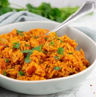 tomato rice in a grey bowl with a fork covered with chopped parsley