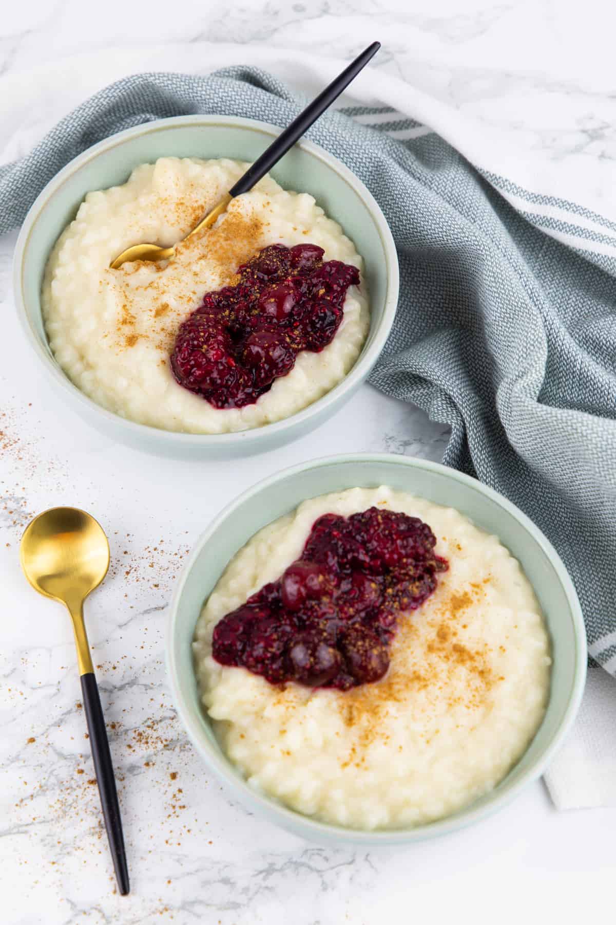 two bowls with rice pudding, cinnamon, and berries on a marble countertop 