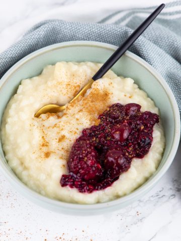 a blue bowl with vegan rice pudding and berries on a marble countertop