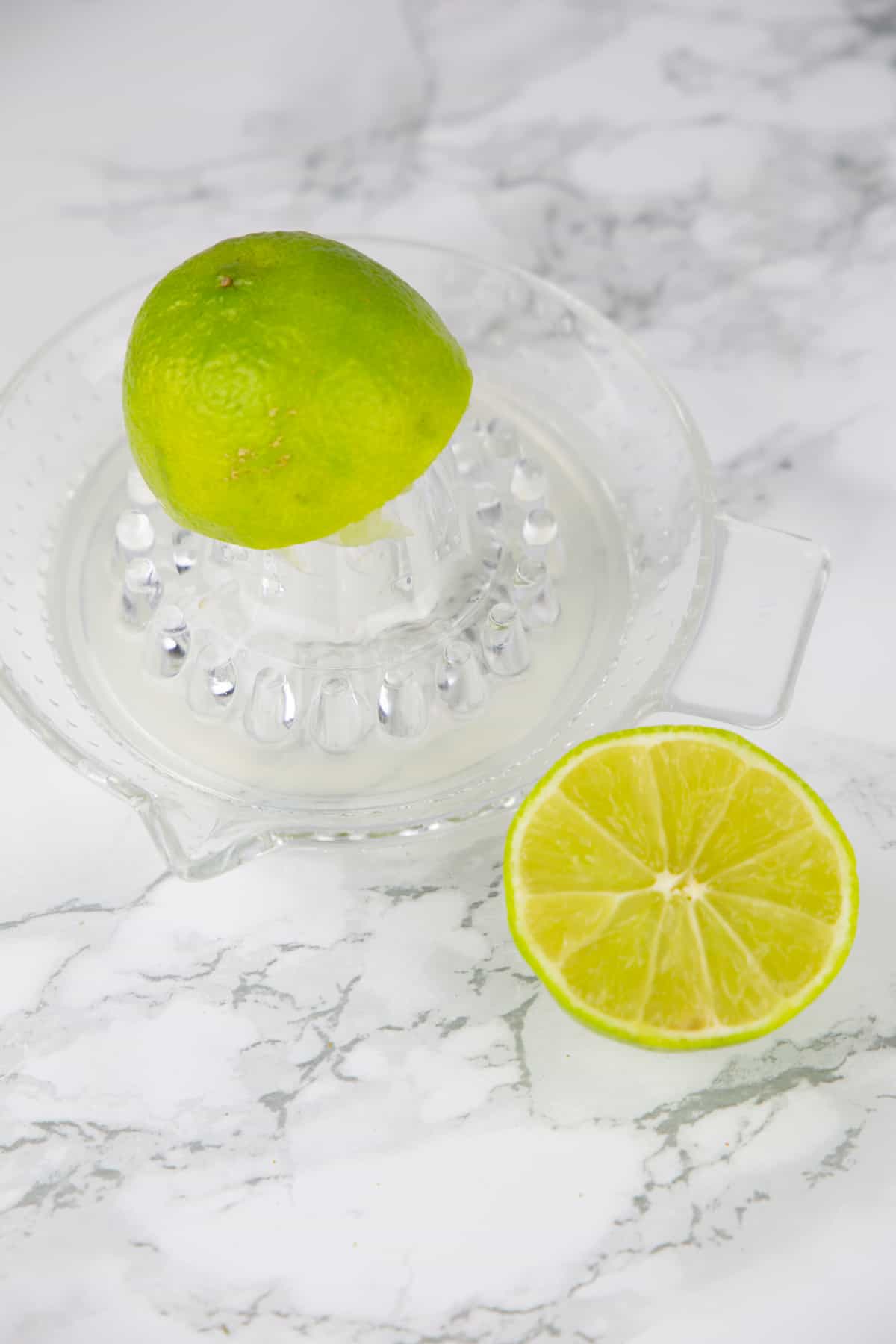 a glass lemon squeezer with two lime halves on a marble countertop