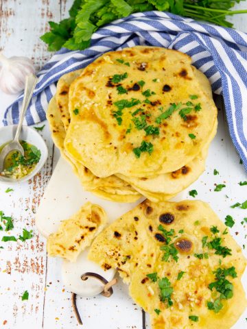 a stack of naan breads sprinkled with chopped parsley on a marble cutting board with garlic in the background