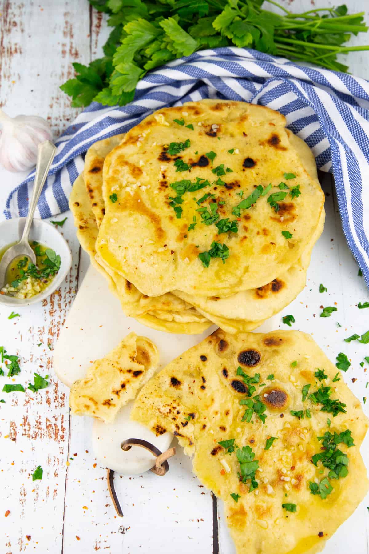 a stack of naan breads sprinkled with chopped parsley on a marble cutting board with garlic in the background 