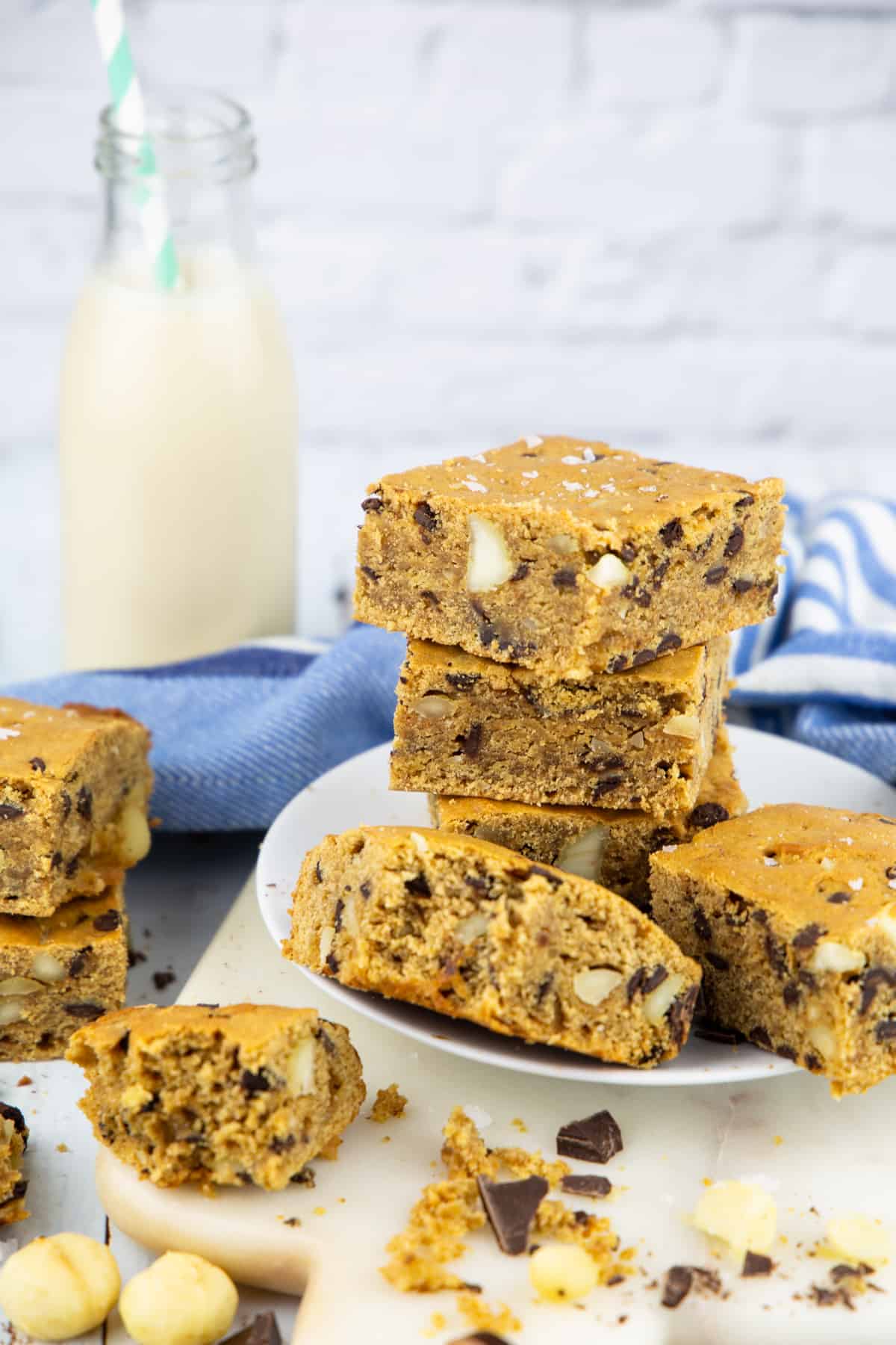a stack of vegan blondies on a white plate with more blondies on the side and a bottle of milk in the background
