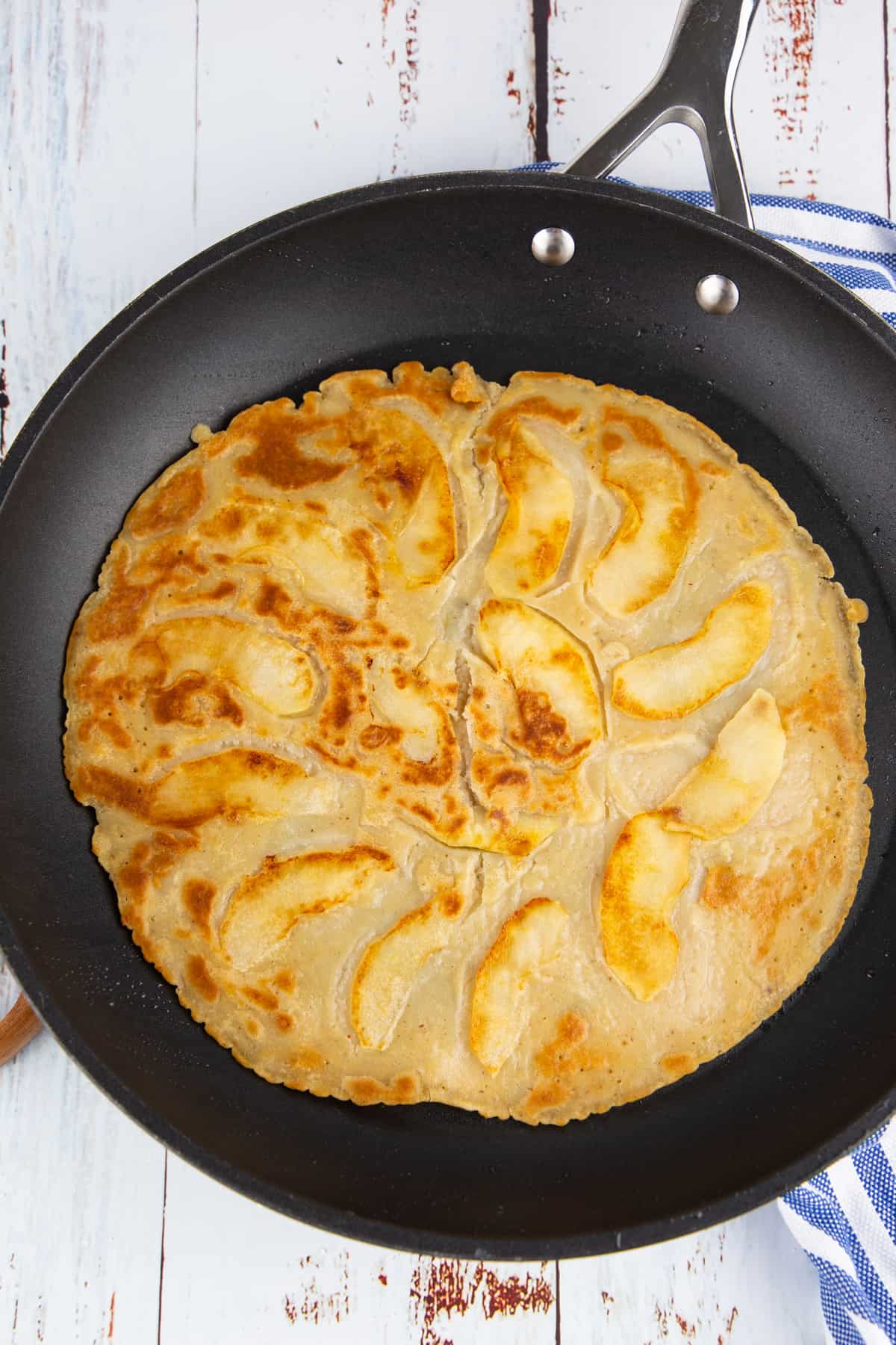 an apple pancake in a large black pan on a wooden board 