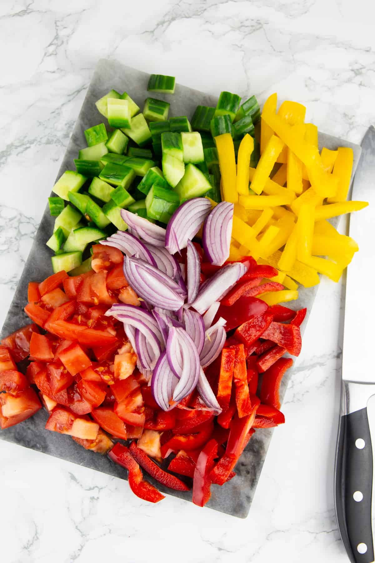 cut up vegetables on a marble chopping board with a knife on the side