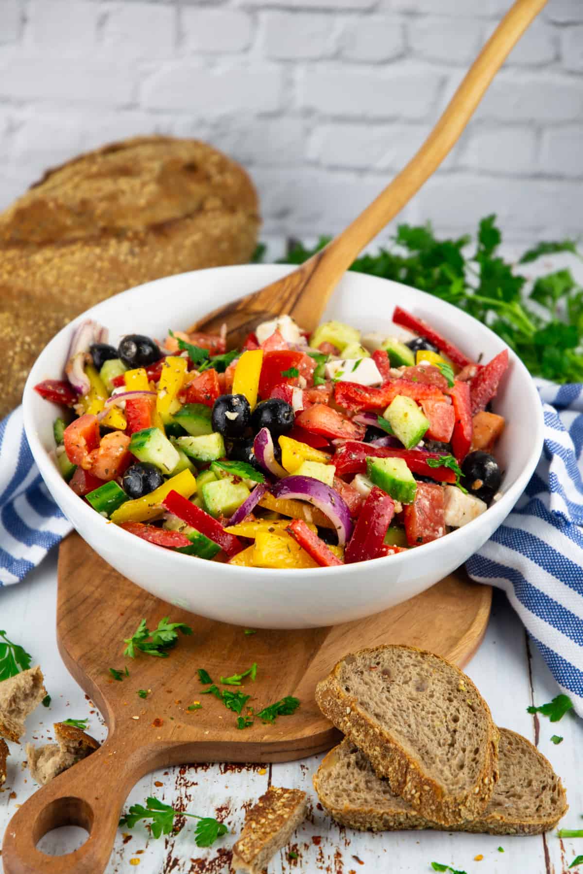 a Greek salad in a white bowl with fresh parsley and bread in the background