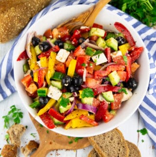 Greek salad in a white bowl with bread on the side