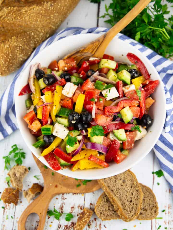 Greek salad in a white bowl with bread on the side