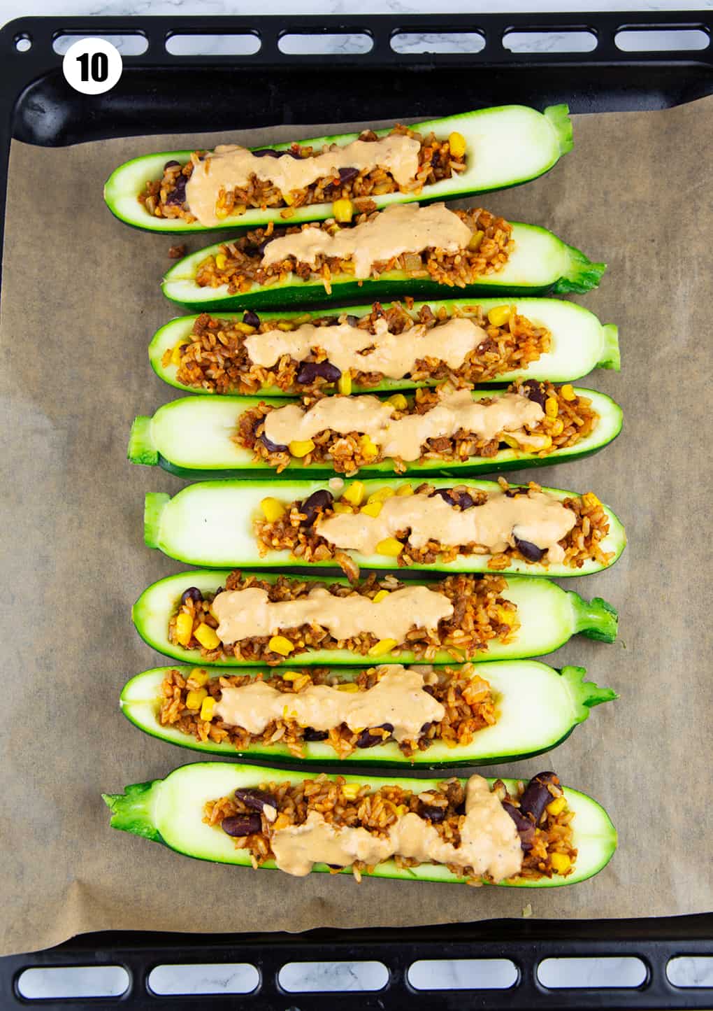 Mexican stuffed zucchini on a baking sheet drizzled with vegan cheese sauce