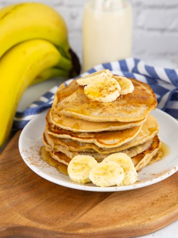 a stack of vegan banana pancakes on a white plate with bananas in the background