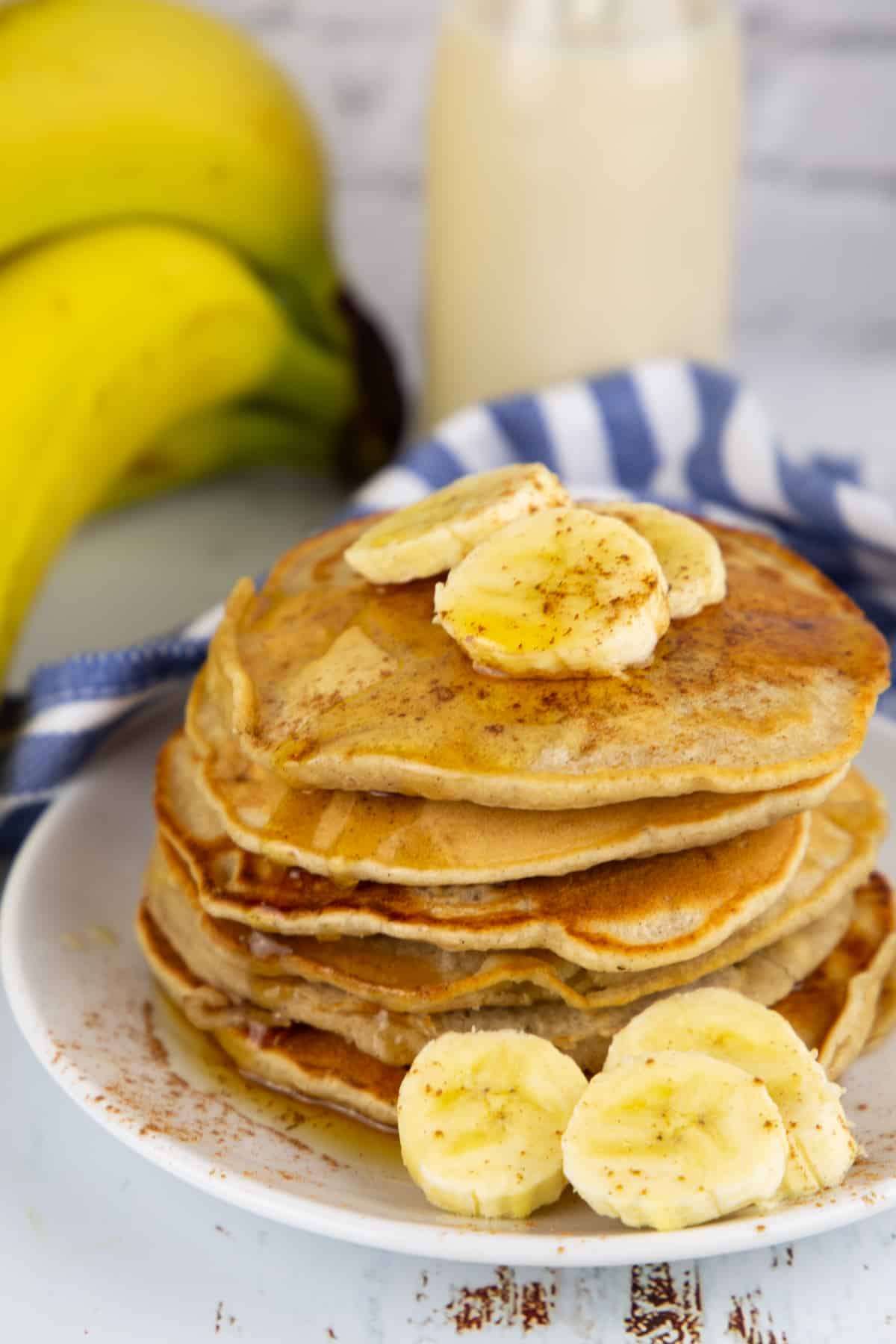 a stack of vegan pancakes with banana slices on a white plate 