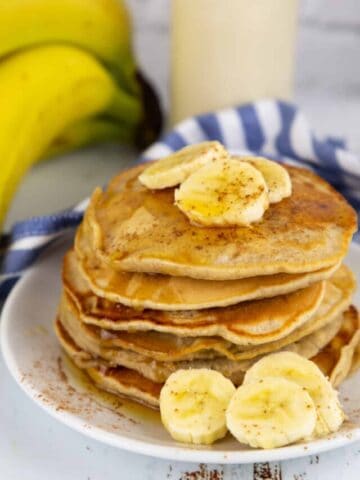 a stack of vegan pancakes with banana slices on a white plate