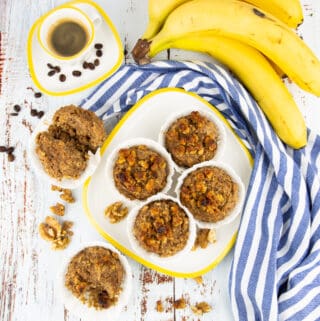 a plate with four banana nut muffins with bananas and a cup with coffee in the background