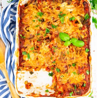 Vegetable lasagna in a white casserole with parsley in the background