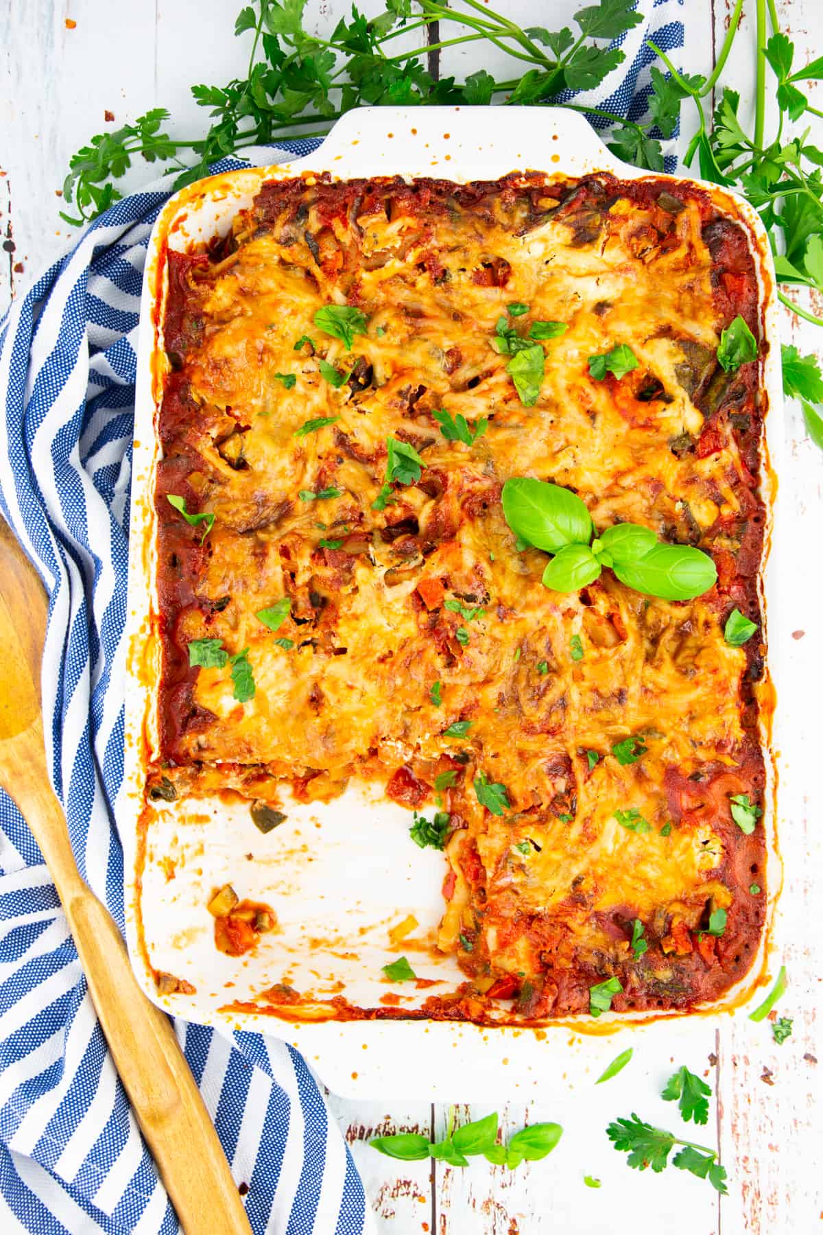 Vegetable lasagna in a white casserole with parsley in the background