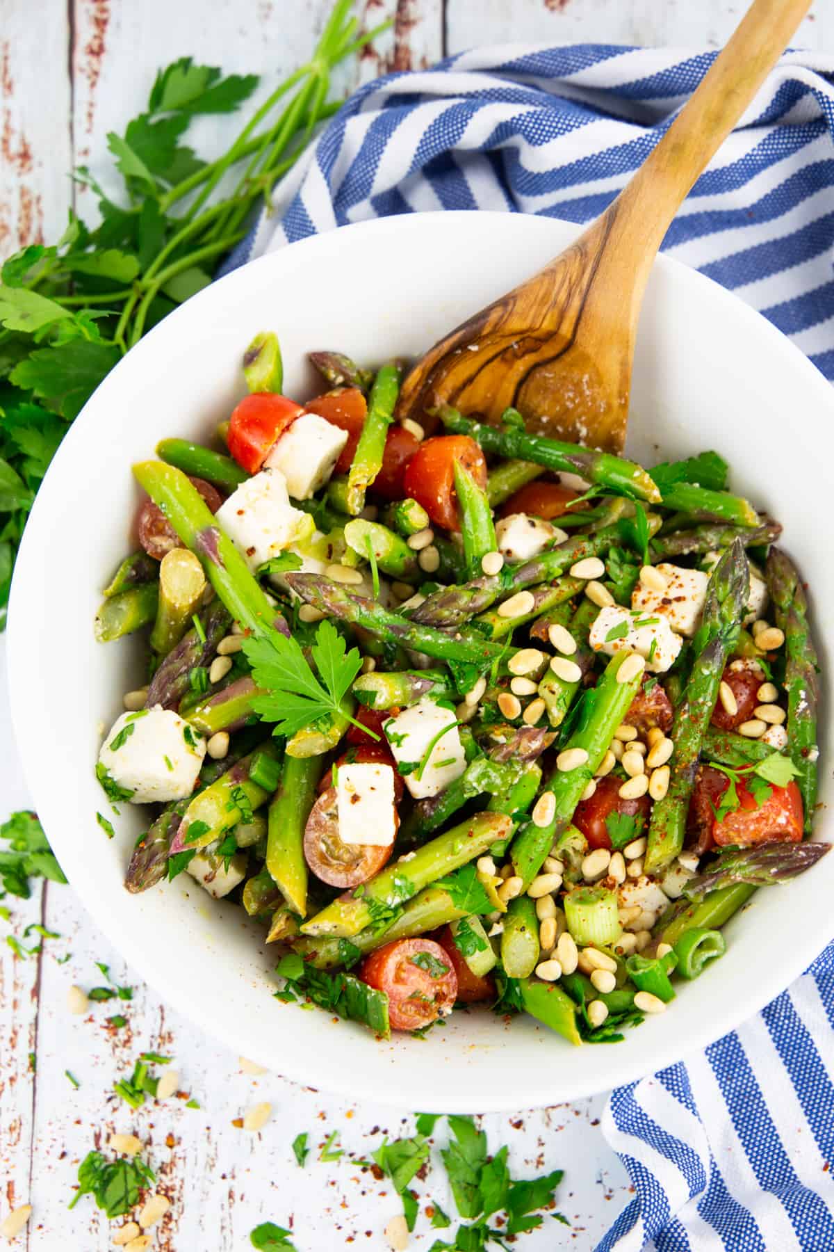 Asparagus Salad with tomatoes in a white bowl with a wooden spoon