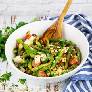 asparagus salad with tomatoes in a white bowl with a wooden spoon
