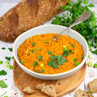 a grey bowl with red lentil soup and a spoon on a wooden board
