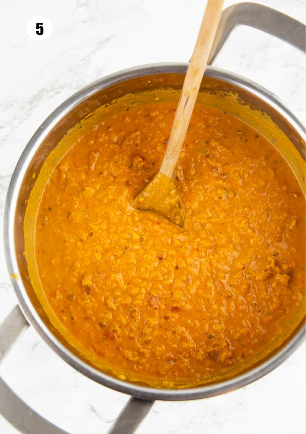 red lentil soup in a pot with a wooden spoon on a marble countertop 