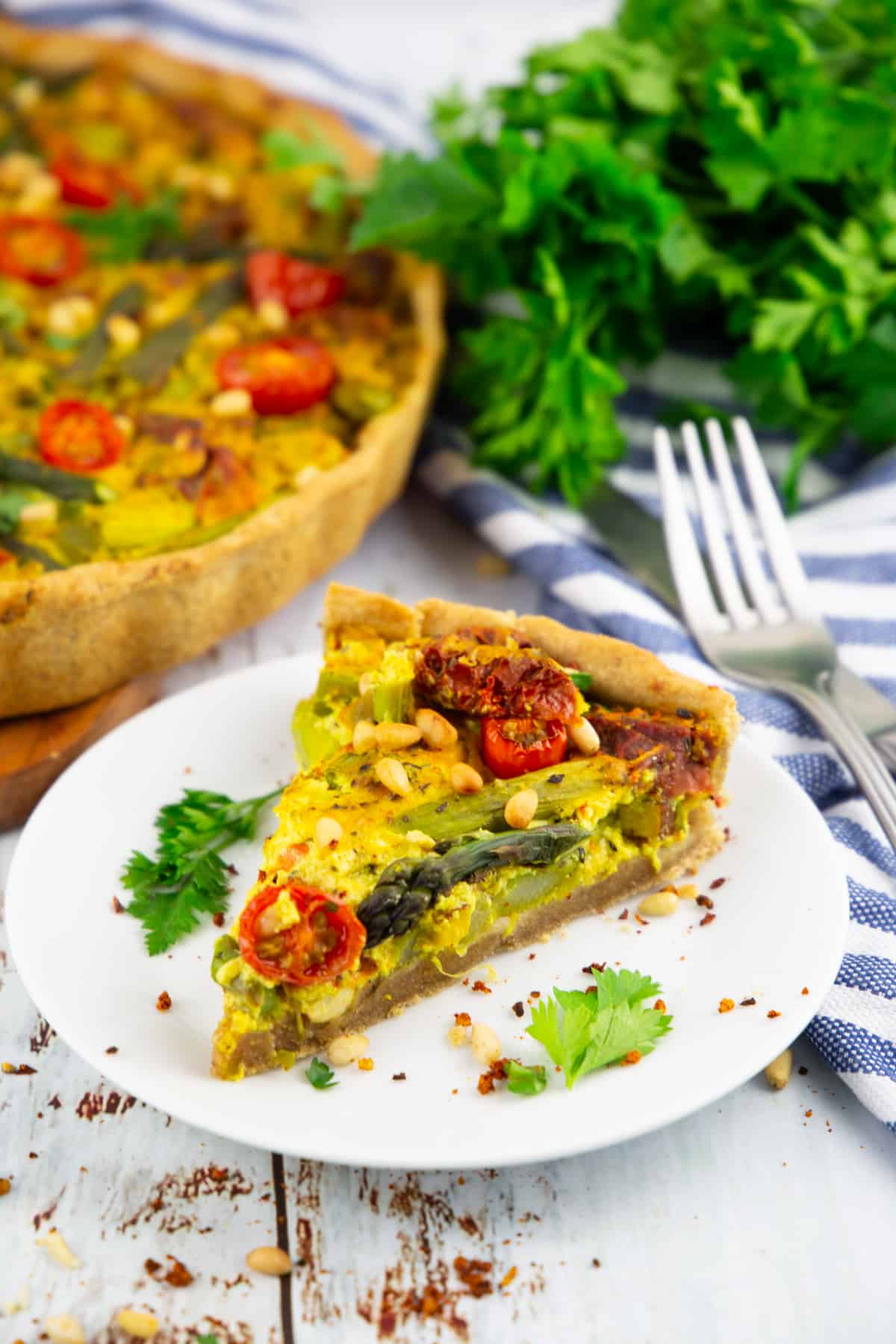 a slice of vegan quiche on a white plate with more quiche in the background