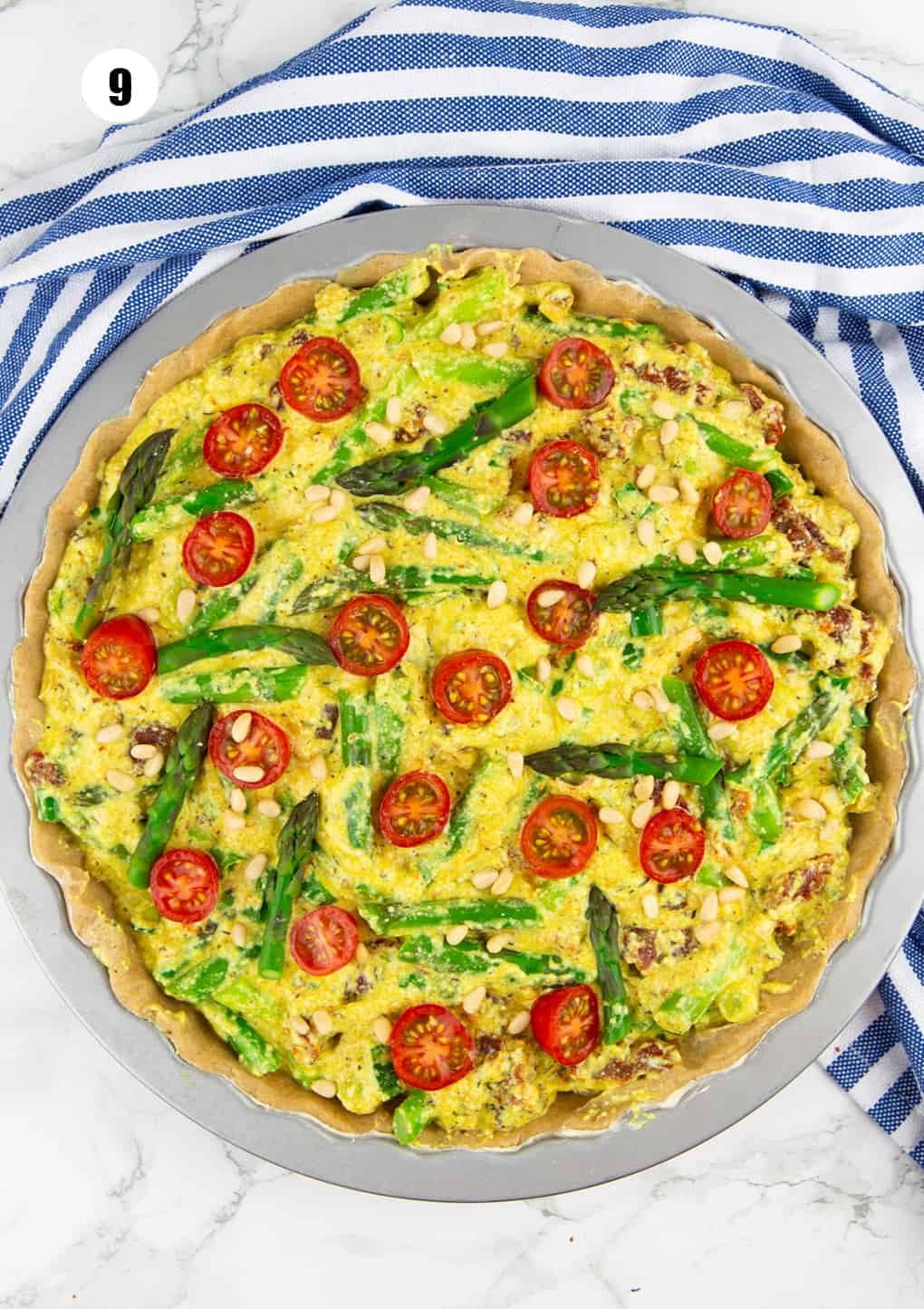 a quiche with tomatoes and asparagus before baking on a marble countertop 