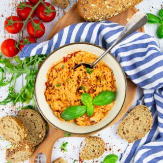 tomato butter in a small bowl on a wooden board with bread, basil, and tomatoes on the side