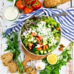 a grey bowl with a green salad with tomatoes and cucumber and a small bowl of yogurt dressing on the side