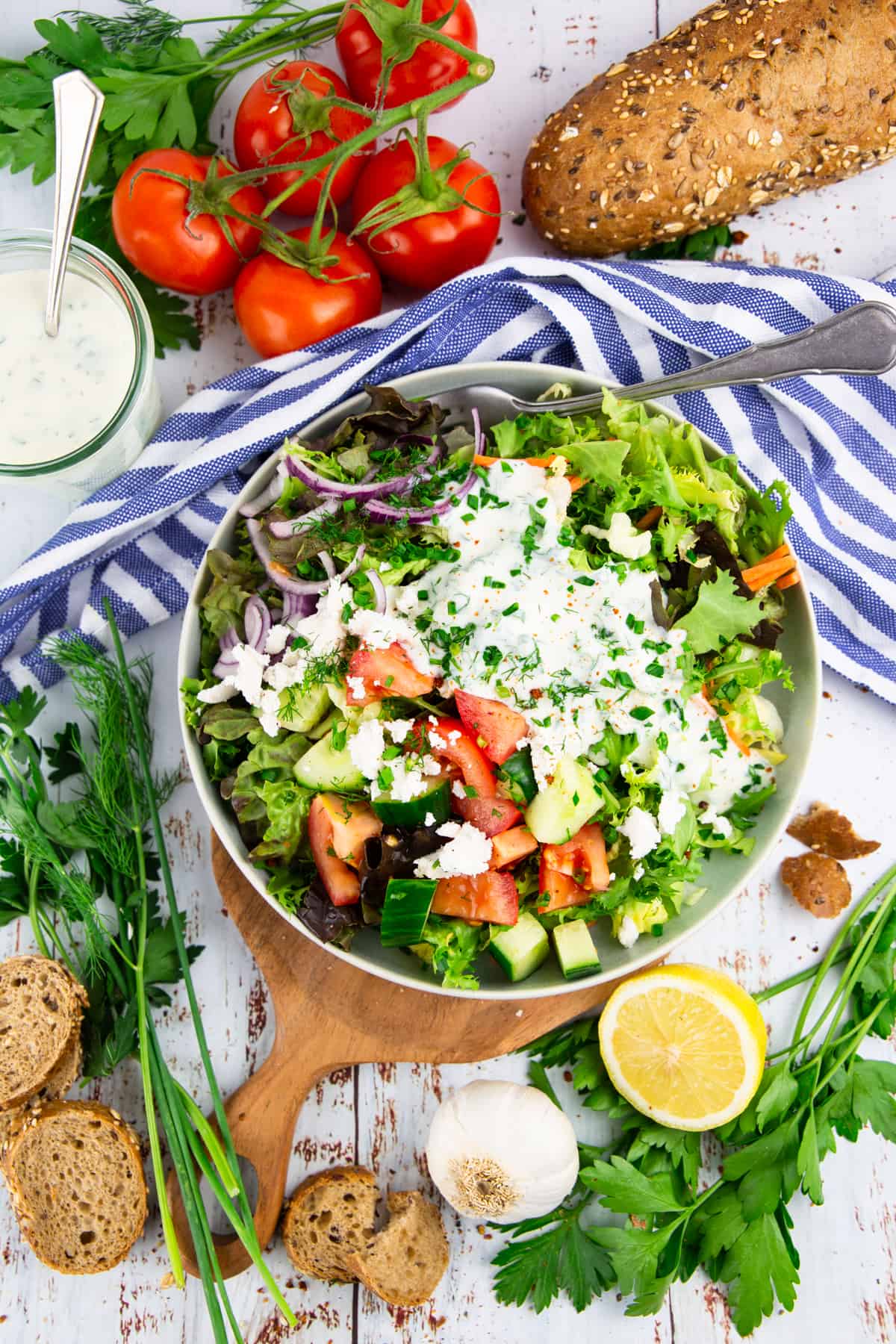 a grey bowl with a green salad with tomatoes and cucumber and a small bowl of yogurt dressing on the side
