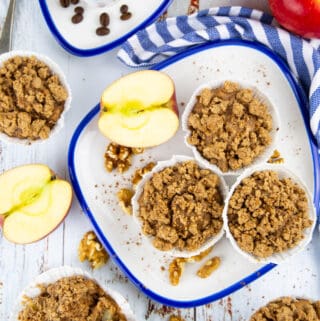 three apple cinnamon muffins on a white plate with a cup of coffee in the background