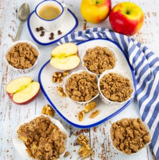 three apple cinnamon muffins on a plate with apples in the background