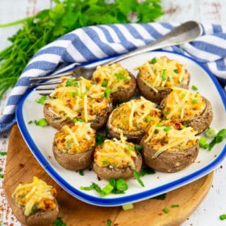 stuffed mushrooms on a white and blue plate on a wooden board with parsley in the background