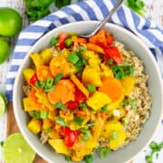 yellow curry with bell pepper and carrots over brown rice in a grey bowl
