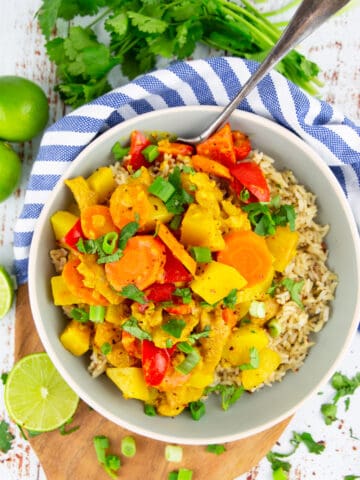 yellow curry with bell pepper and carrots over brown rice in a grey bowl