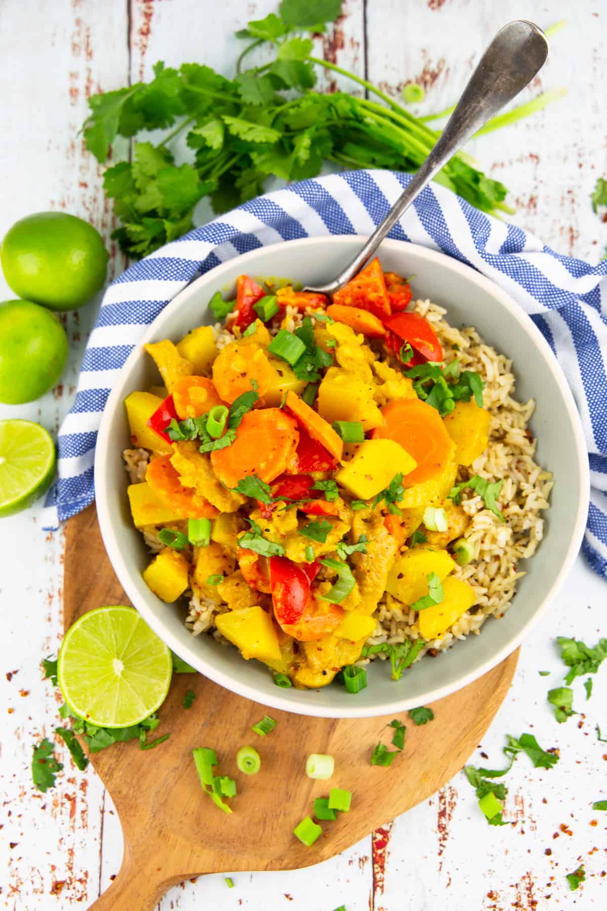 a grey bowl with yellow curry on a wooden board with limes and cilantro in the background 