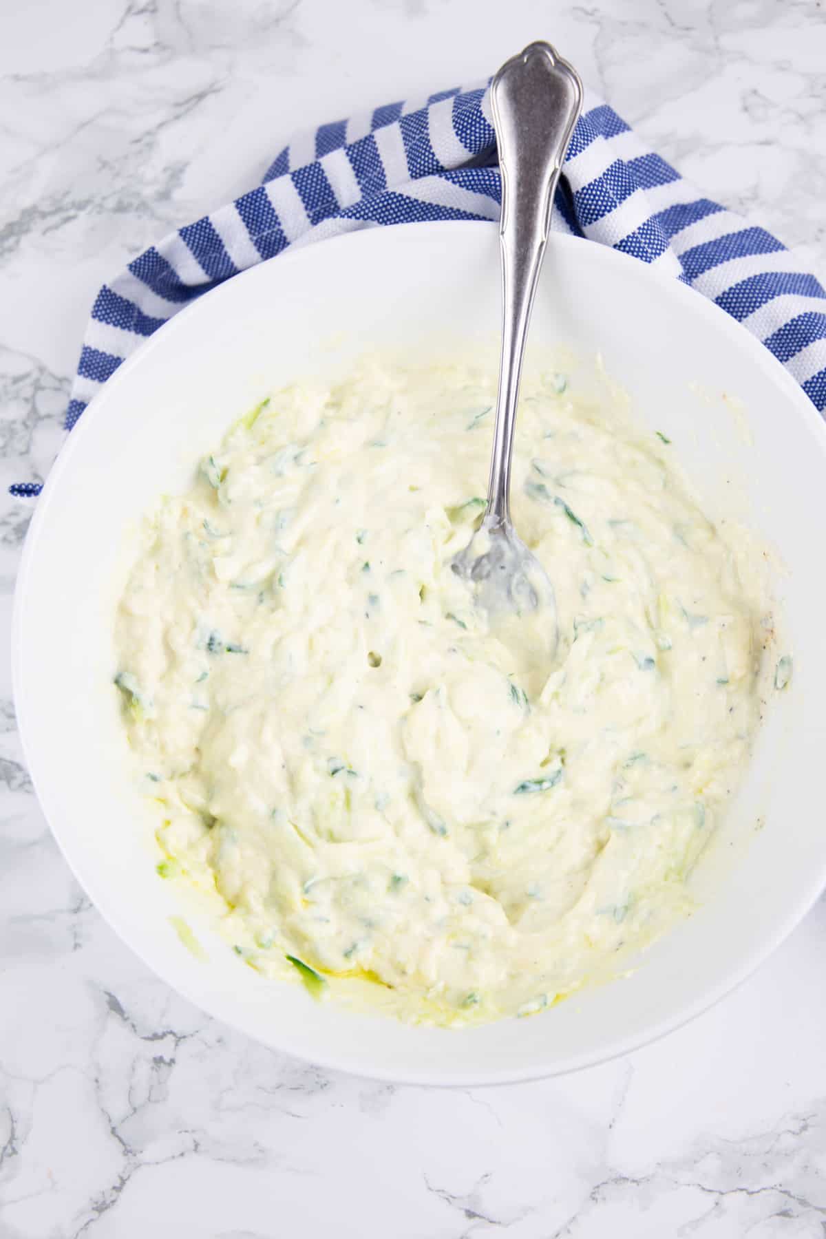 vegan tzatziki in a white bowl with a spoon on a marble countertop 