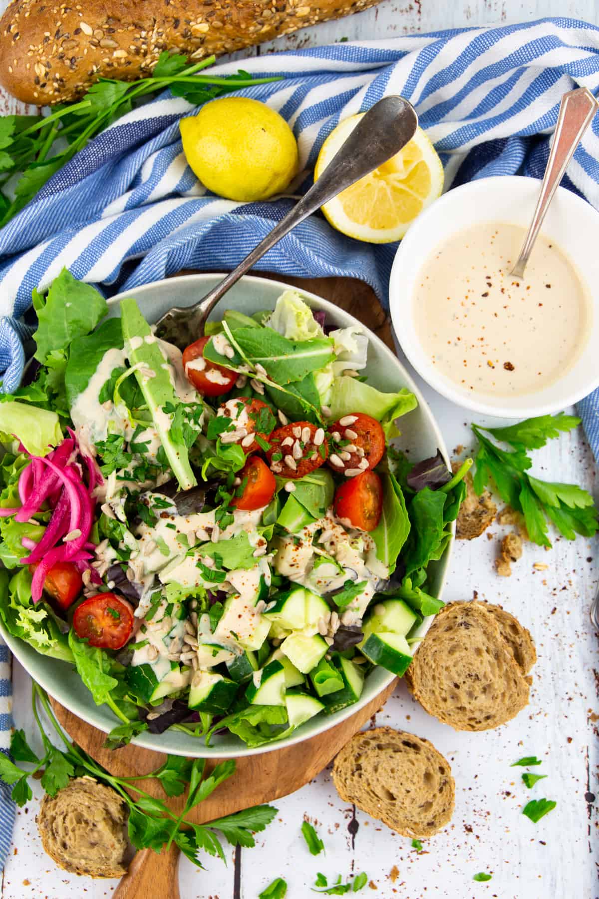 a big bowl with salad on a white wooden board with a bowl of tahini dressing on the side 