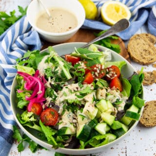 a green salad with tomatoes with a small bowl of lemon tahini dressing in the background