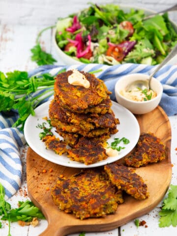 a stack of lentil burgers on a white plate with a bowl of salad in the background